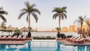 A poolside area with lounge chairs and umbrellas, overlooking a body of water with a cityscape in the background.