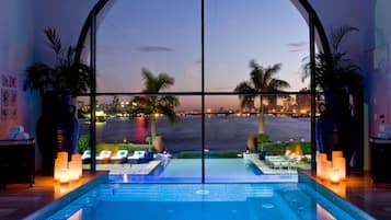 A pool area with a view of a city skyline at dusk, lounge chairs, and candles.