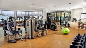 A gym with various exercise machines, a green Reebok ball, and a view of a cityscape through large windows. - Sofitel Cairo Nile El Gezirah (Cairo)