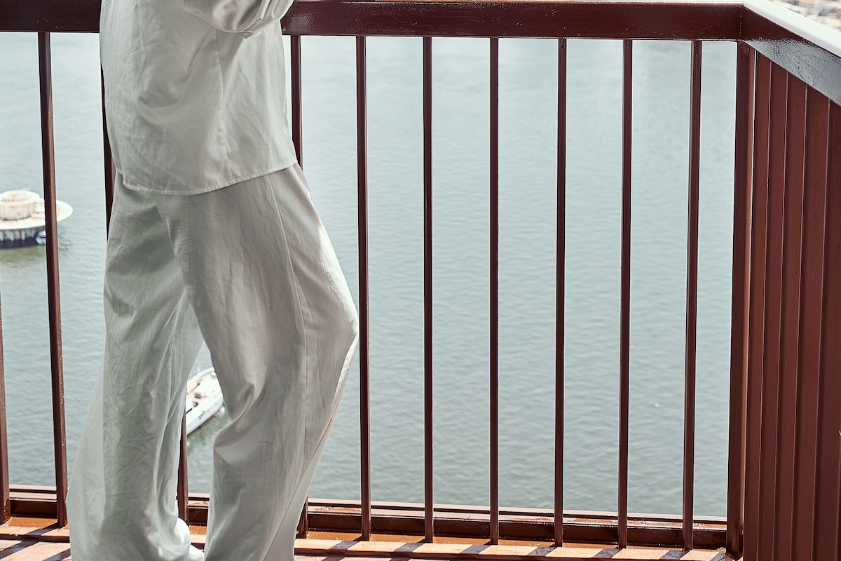 A person standing on a balcony with a view of a city skyline and a body of water.