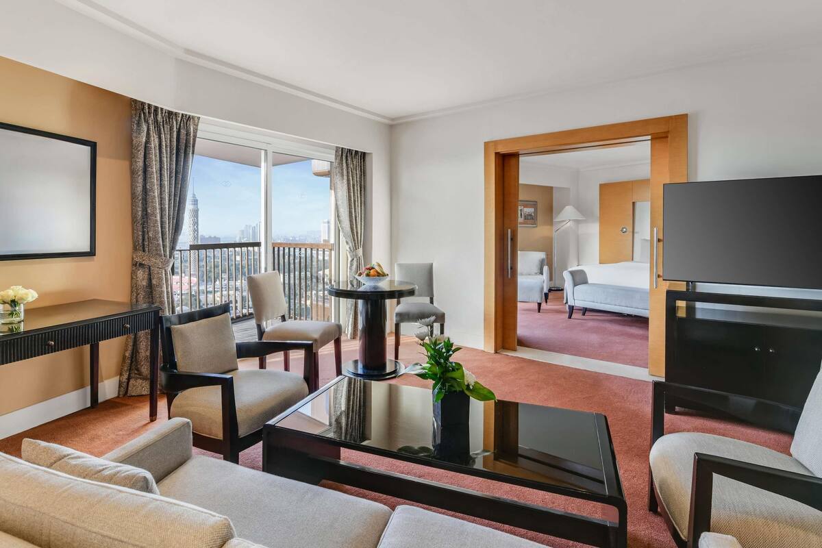 A hotel room with a balcony, a TV, a desk, and a bed.