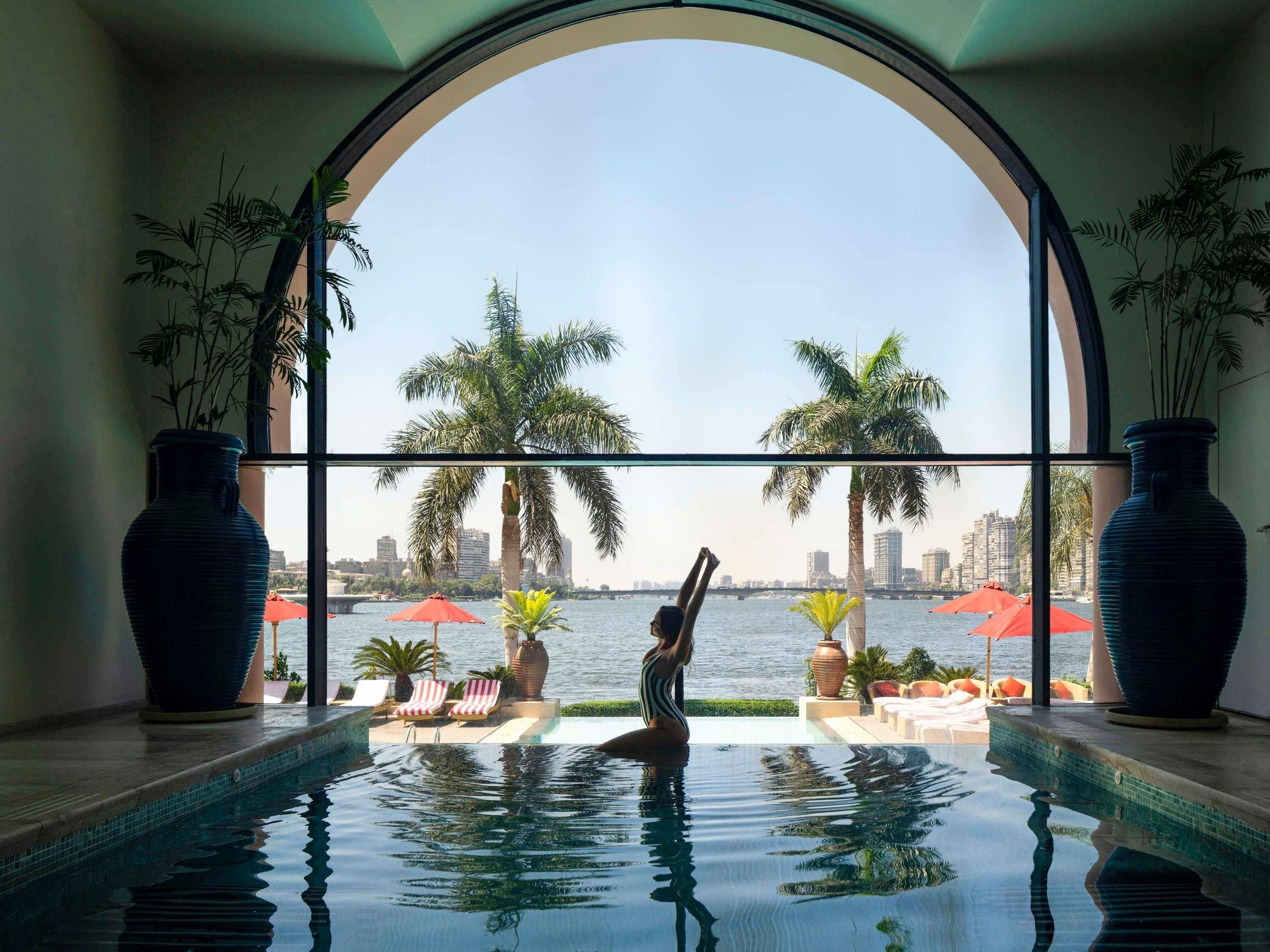 Piscina con vista al horizonte urbano, palmeras y sillas de descanso.