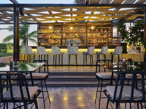 Una zona de bar con mostrador, taburetes y una variedad de botellas.