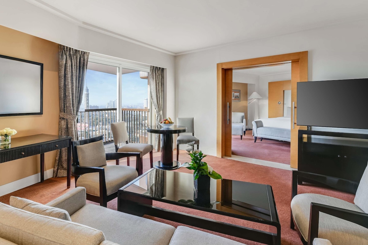 A hotel room with a balcony, a TV, a desk, and a bed.