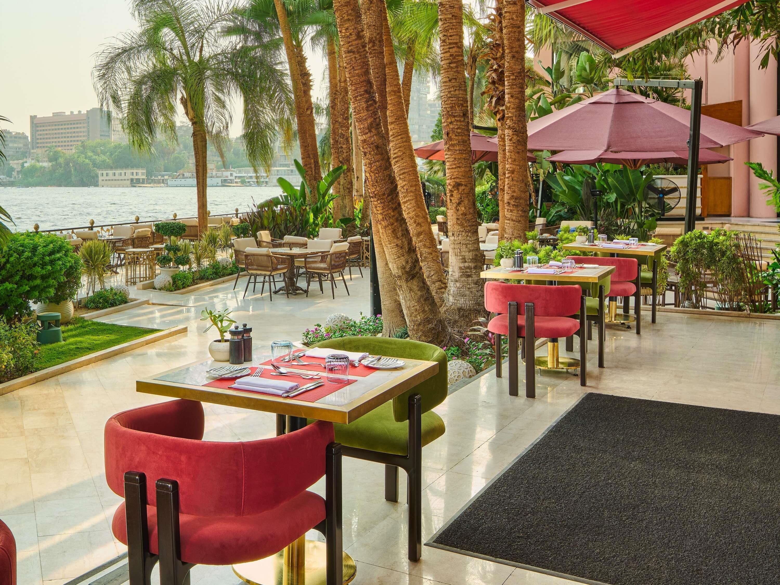 A waterfront restaurant with outdoor seating, palm trees, and a view of the water.