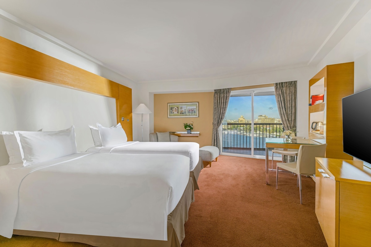 A hotel room with a bed, a desk, a television, and a view of the city.