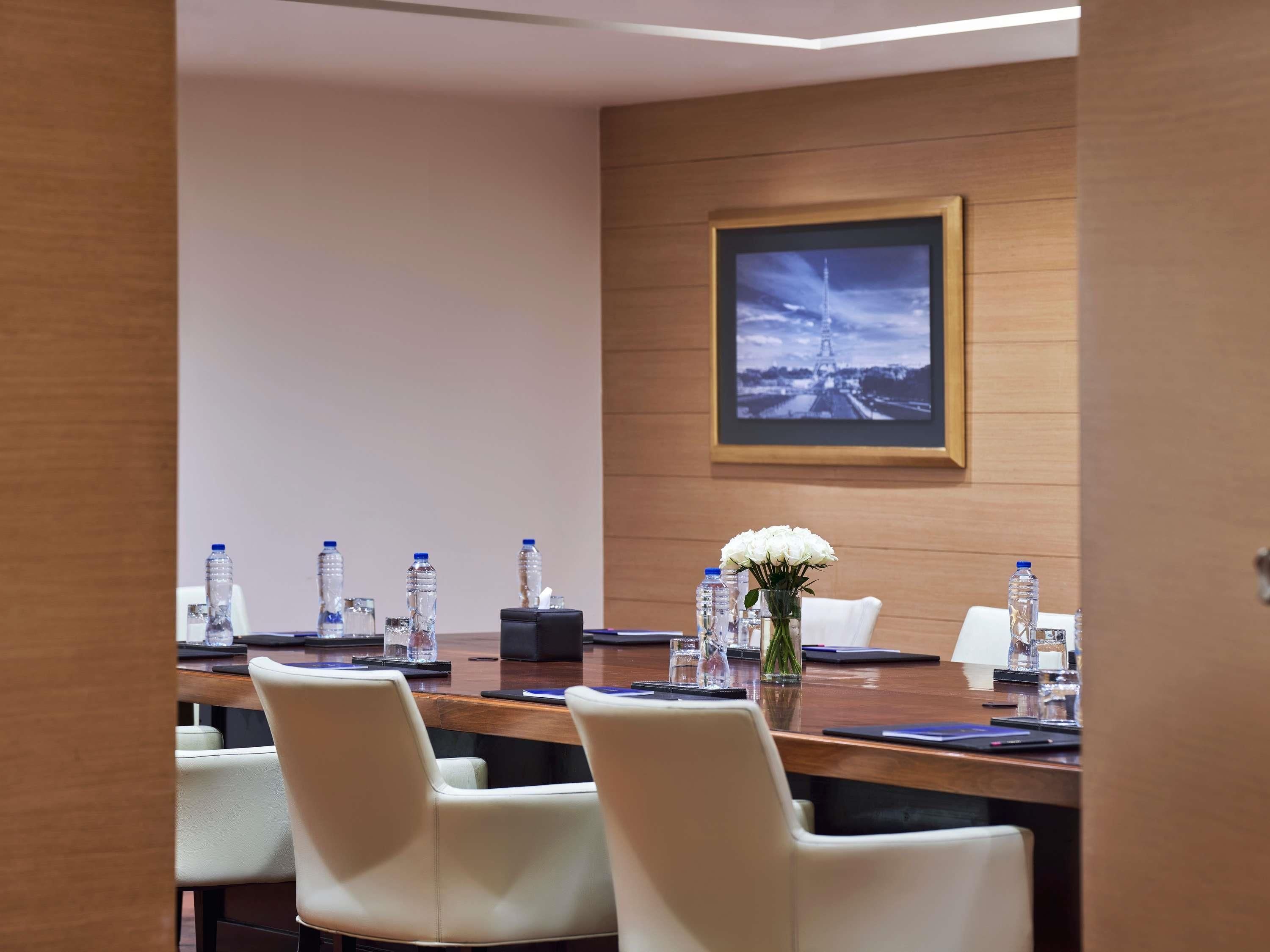A conference room with a long table, chairs, water bottles, a vase with flowers, and a framed picture on the wall.