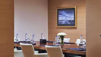 A conference room with a long table, chairs, water bottles, a vase with flowers, and a framed picture on the wall.