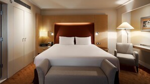 A hotel room with a large bed, a desk, a chair, and a wardrobe.