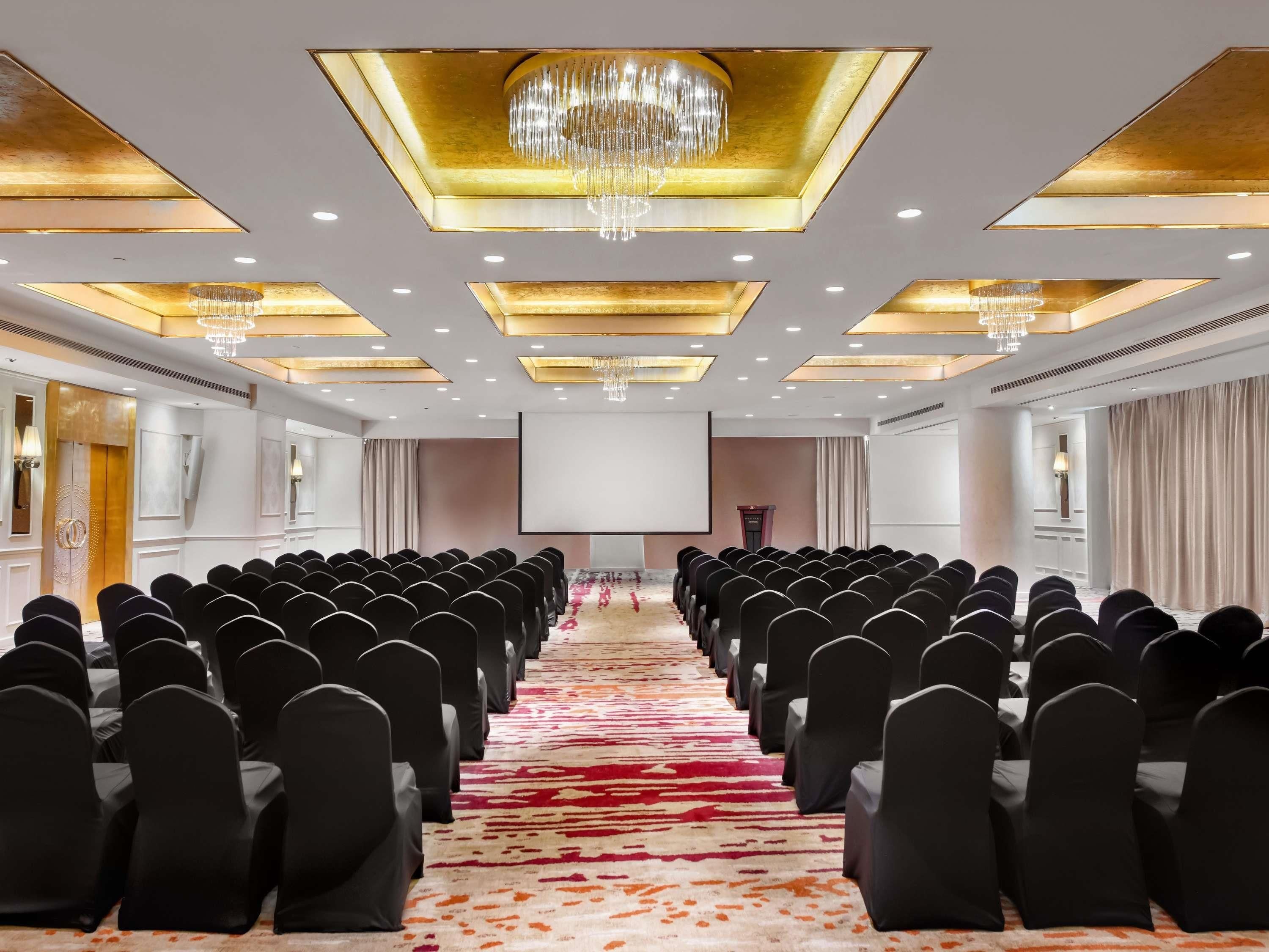 A conference room with rows of chairs, a large screen, and chandeliers.