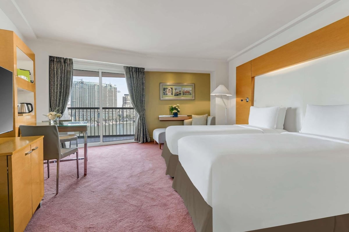 Ein Hotelzimmer mit Bett, Schreibtisch, Stuhl, Fernseher, Lampe und Blick auf die Stadt.