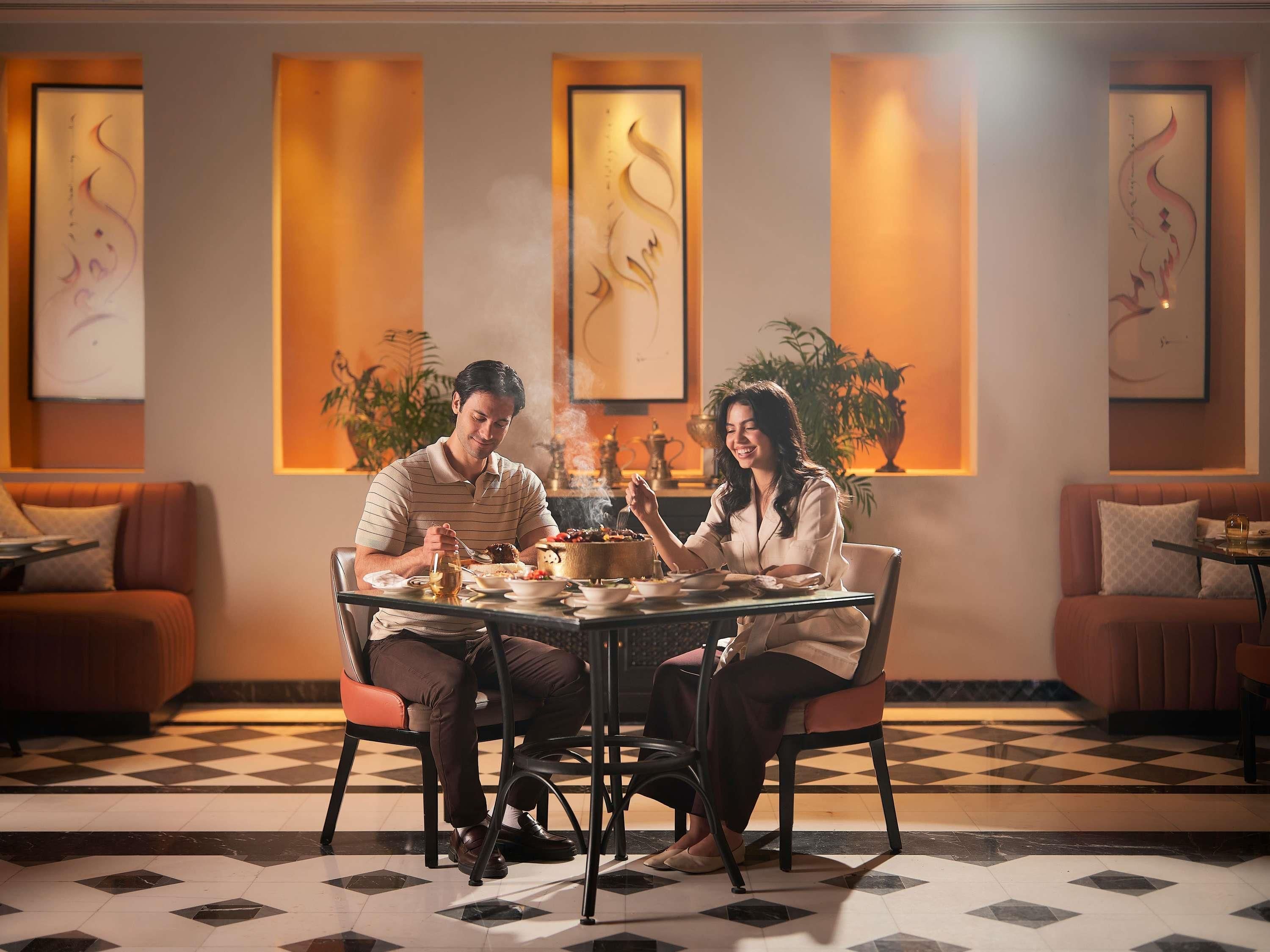 A dining area with a checkered floor, a round table, and two people seated.