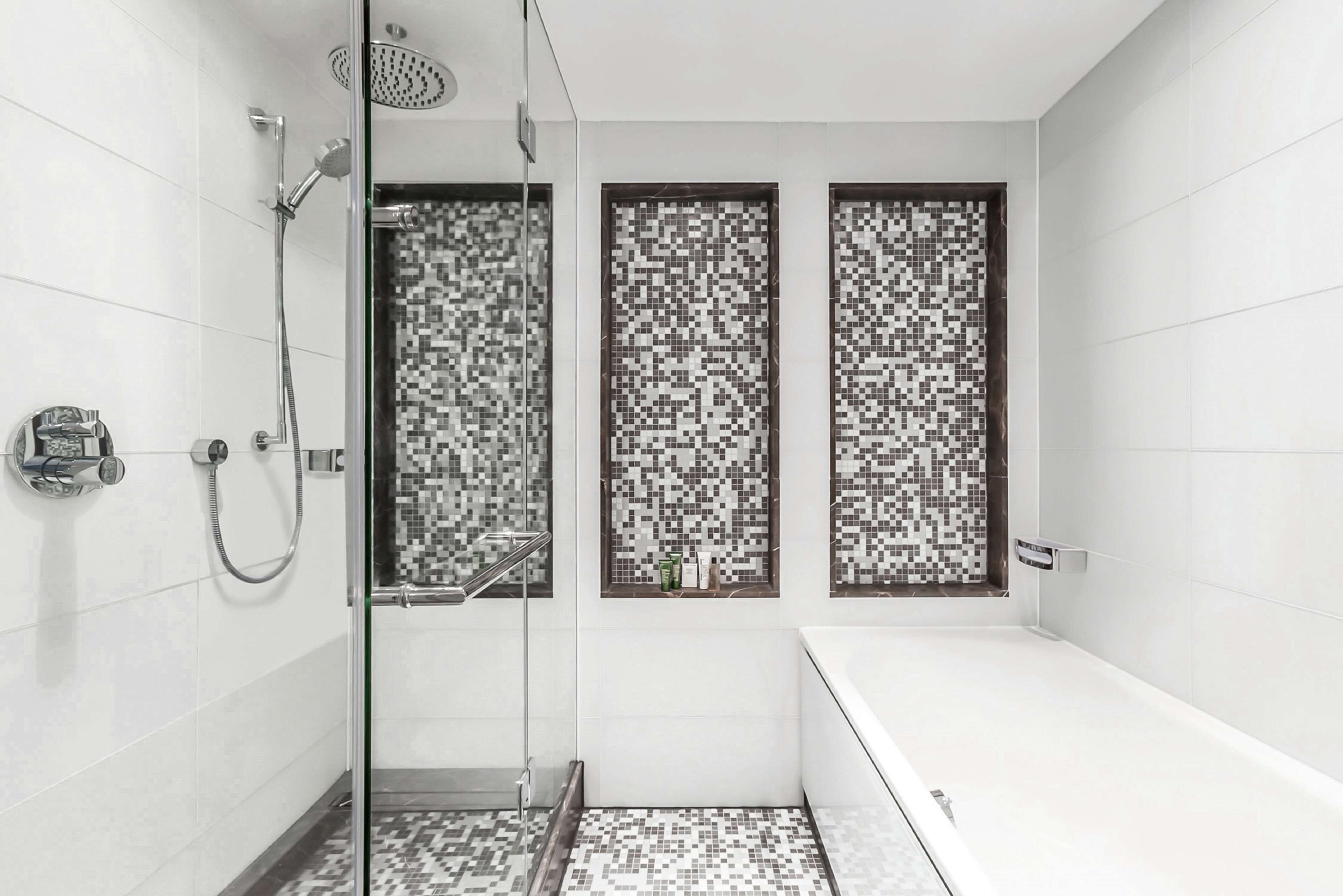 A modern bathroom with a glass-enclosed shower, a white bathtub, and mosaic-patterned windows.