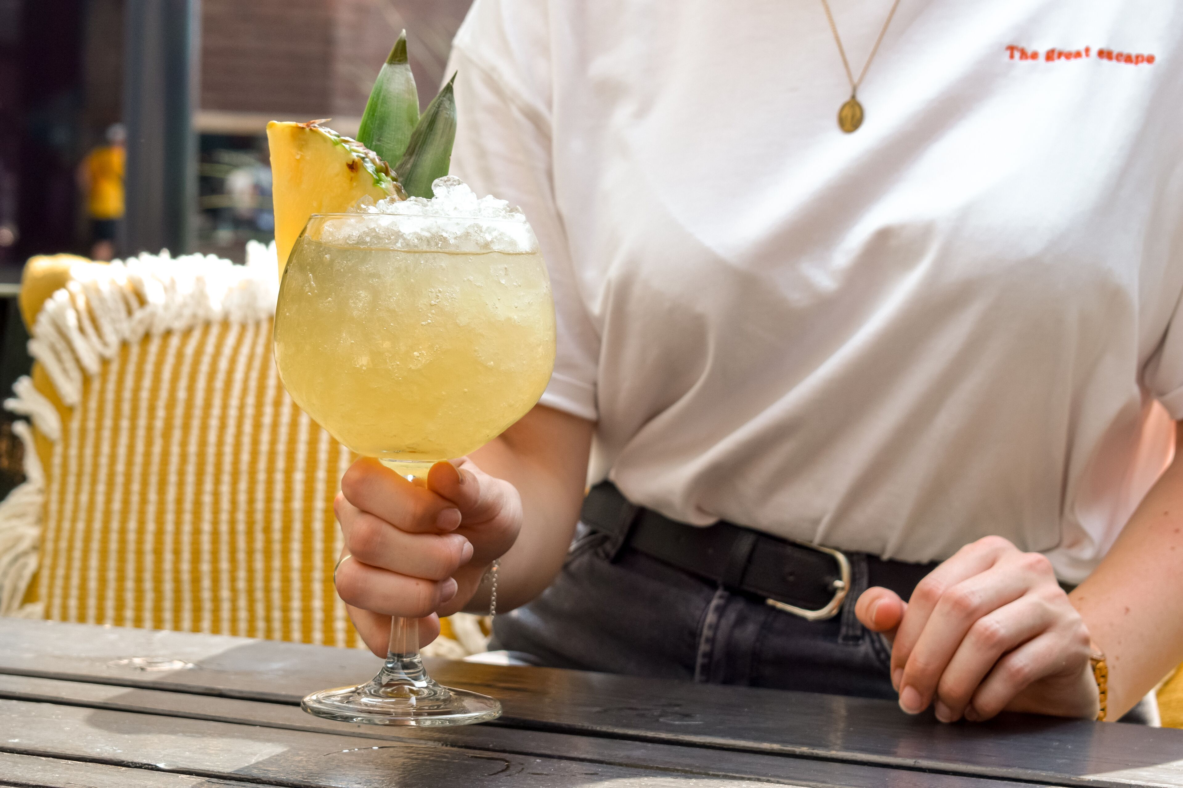 Une personne tenant un cocktail décoré d’une tranche d’ananas sur une table en bois.