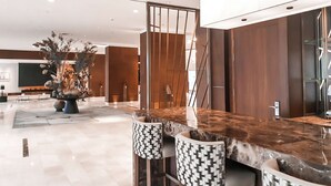 A modern hotel lobby with a marble reception desk, two patterned bar stools, a large decorative plant, and a wooden partition. - Hilton Rotterdam (Rotterdam)