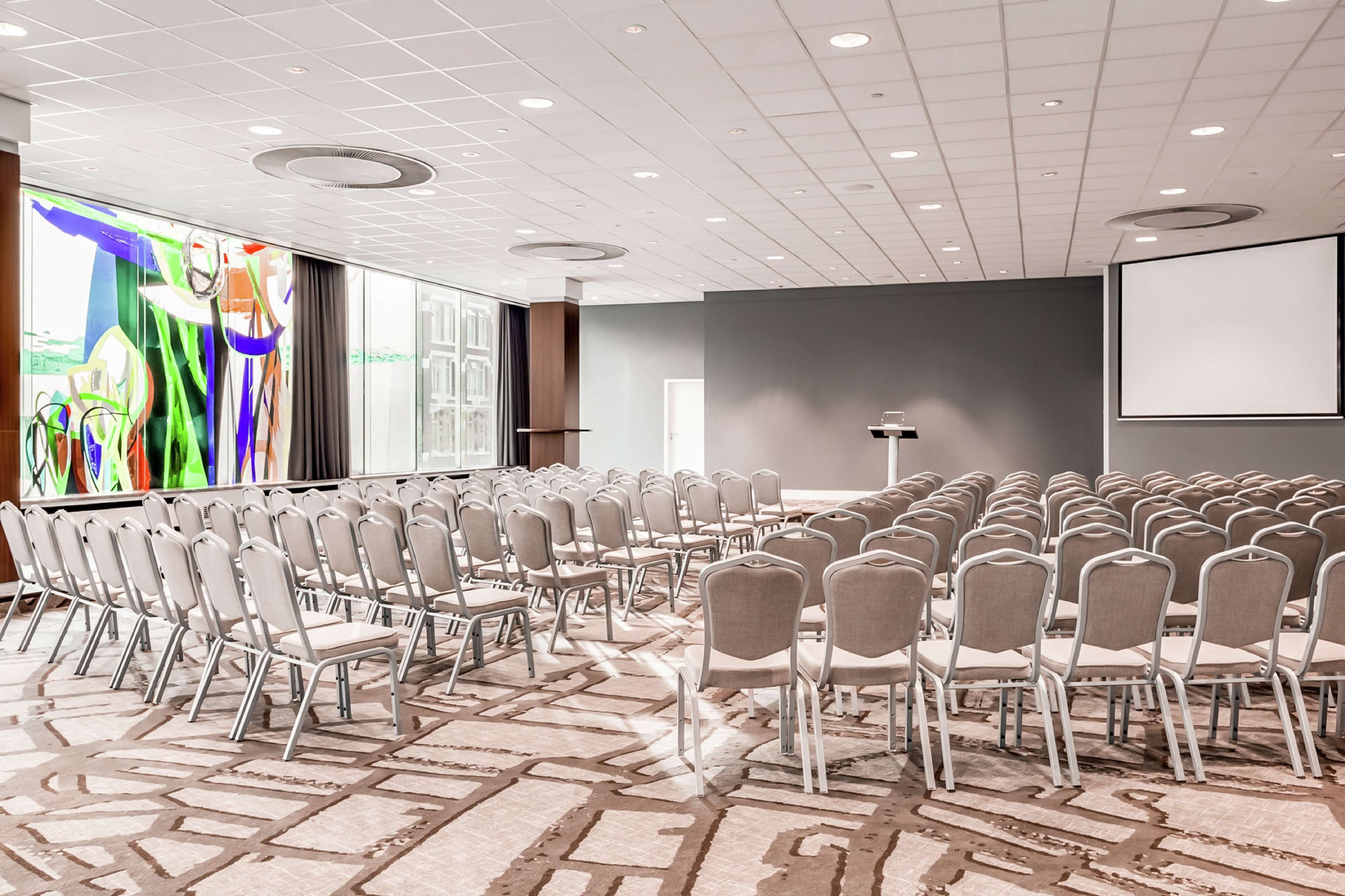 A conference room with rows of chairs, a large screen, and a projector.