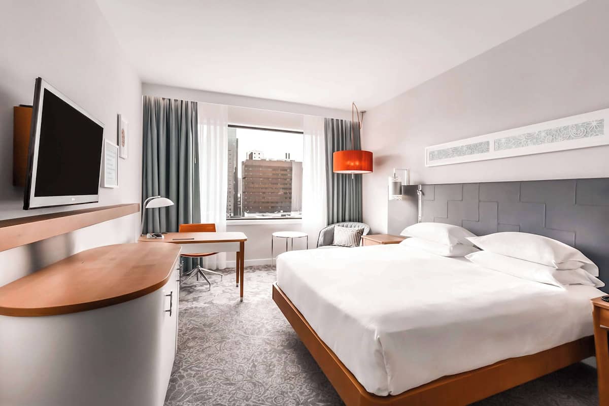 A hotel room with a bed, desk, chair, and a TV.