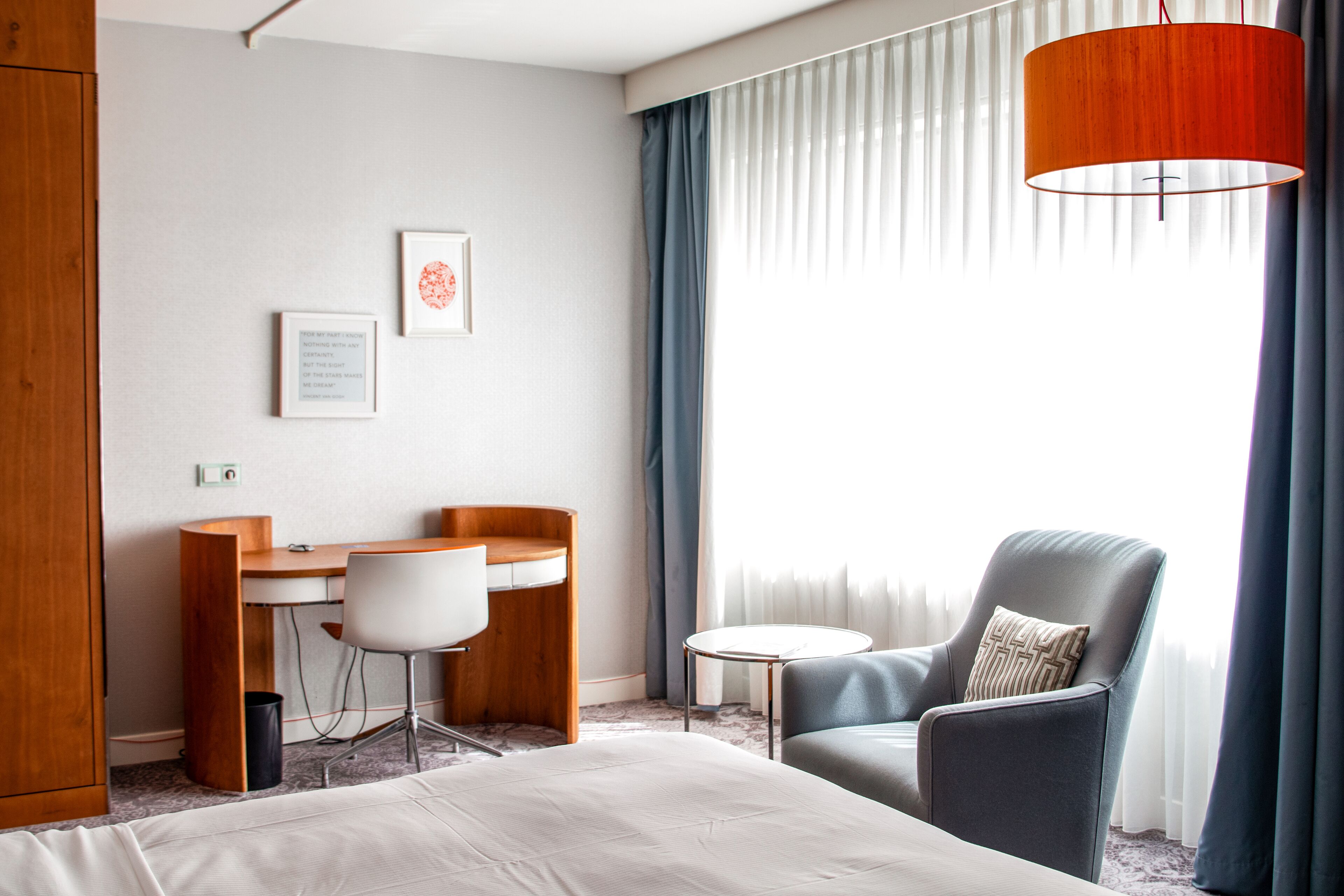 A hotel room with a bed, a desk, a chair, and a lamp.