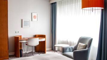 A hotel room with a bed, a desk, a chair, and a lamp.
