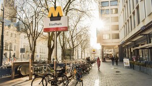 A city street with a bike parking area, a sign for 'Stadhuis', and a tram line.