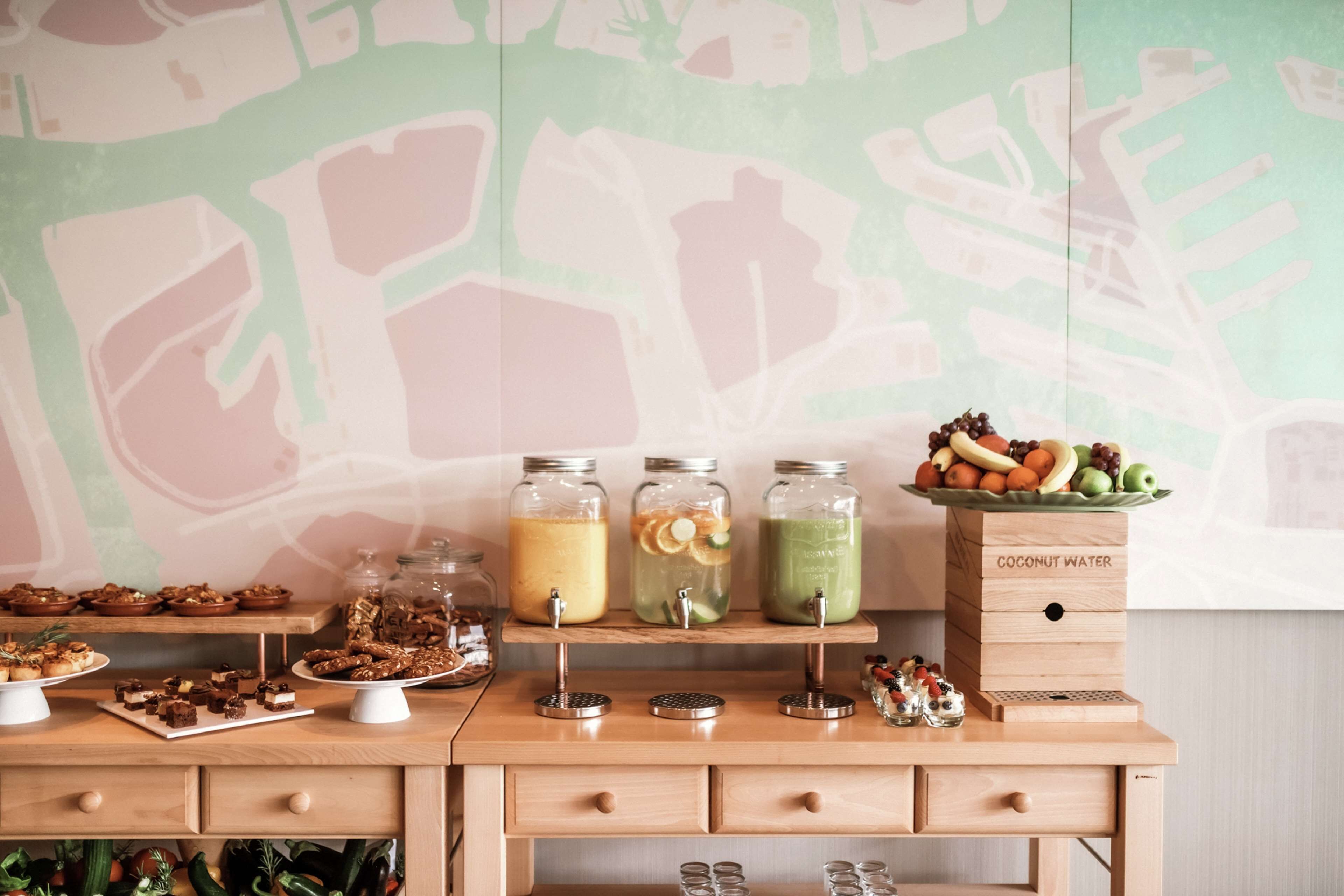 Una mesa buffet de madera con diferentes alimentos y bebidas, incluyendo frascos de batidos y una caja con la etiqueta 'Agua de Coco'.
