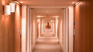 A hotel hallway with wooden doors, a carpeted floor, and wall-mounted lighting.