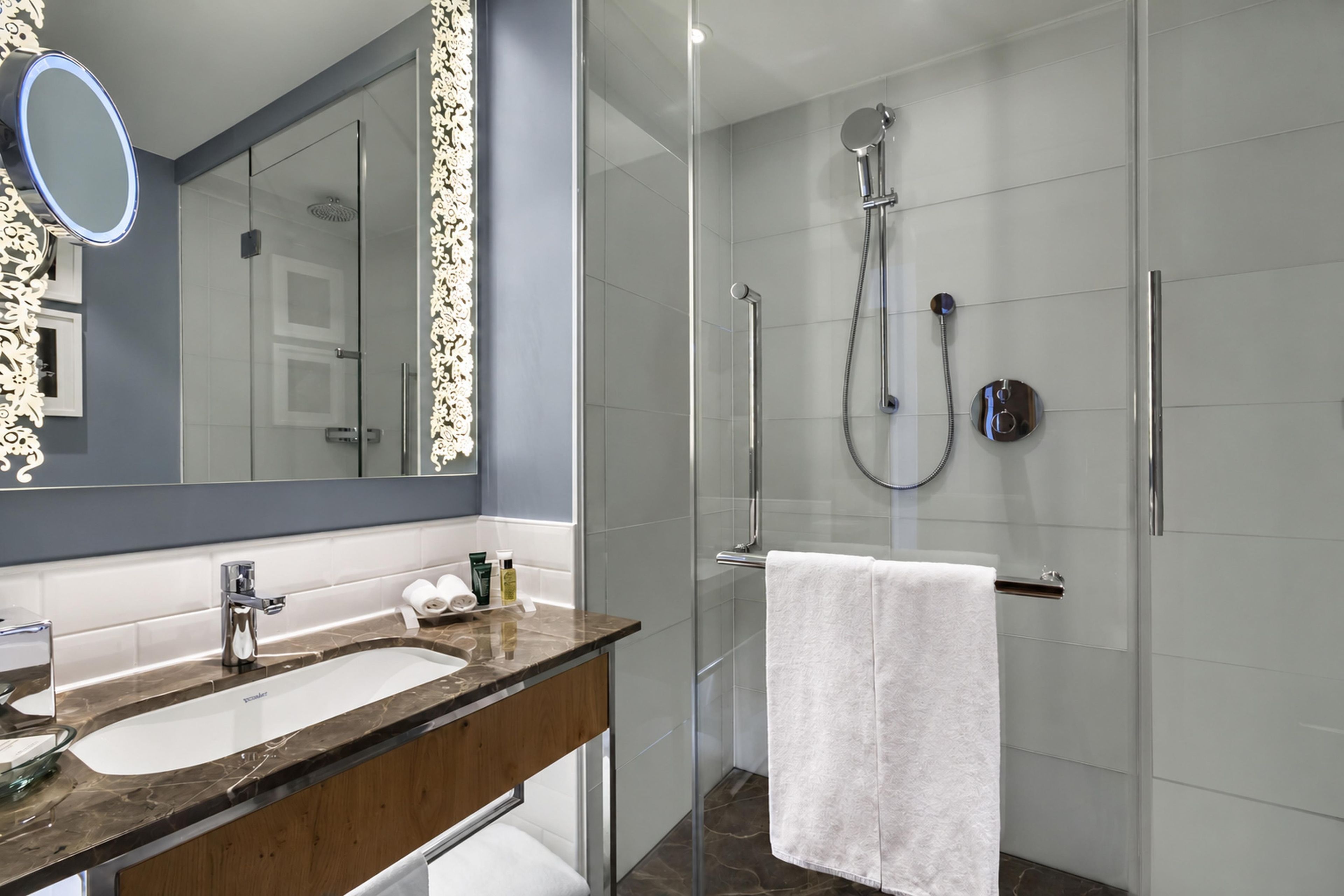 Une salle de bain moderne dotée d’une douche à parois de verre, d’un meuble-lavabo avec un plan de travail en marbre et d’un grand miroir encadré.
