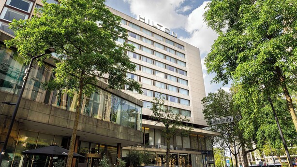 A modern hotel building with a glass facade, multiple floors, and a visible "Hilton" sign.