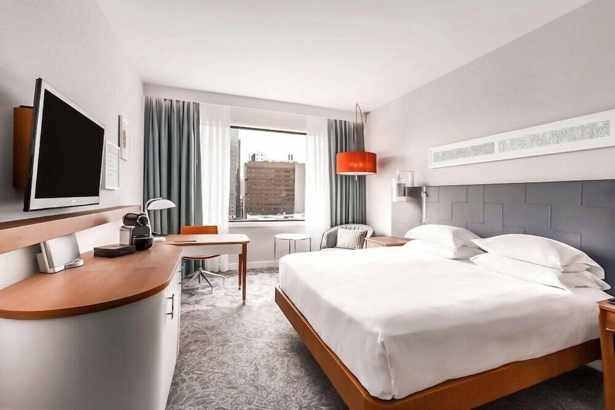 A hotel room with a bed, a desk, a chair, a television, and a window with curtains.