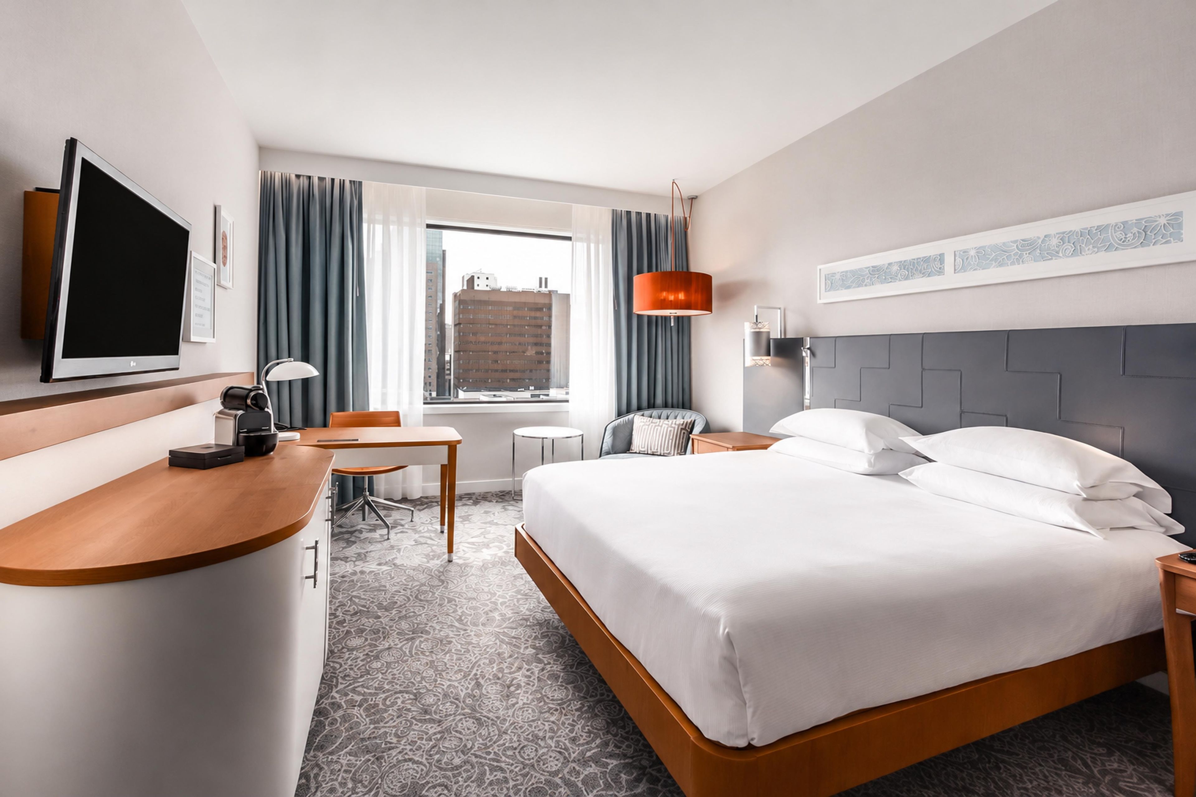 A hotel room with a bed, desk, chair, and a television.
