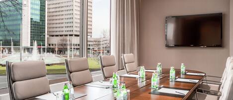 A conference room with a long table, multiple chairs, and a large screen.