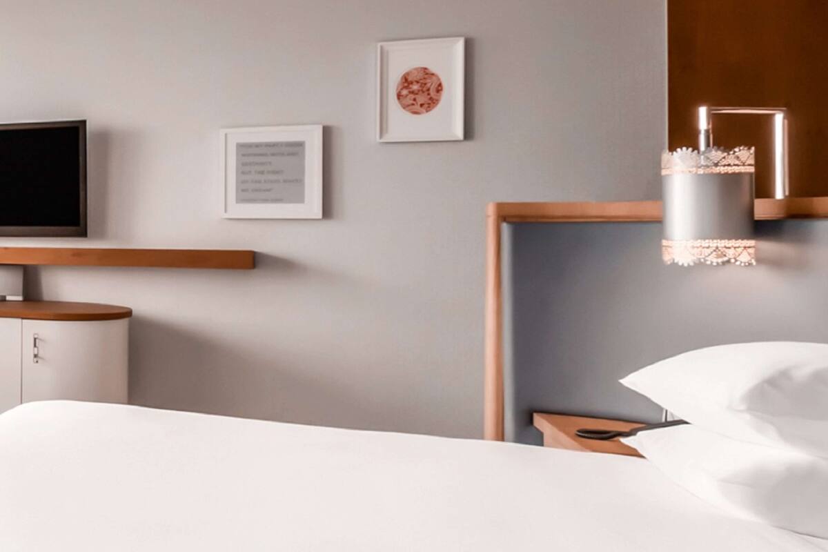 A modern hotel room with a bed, a bedside table, a TV, and framed artwork on the wall.