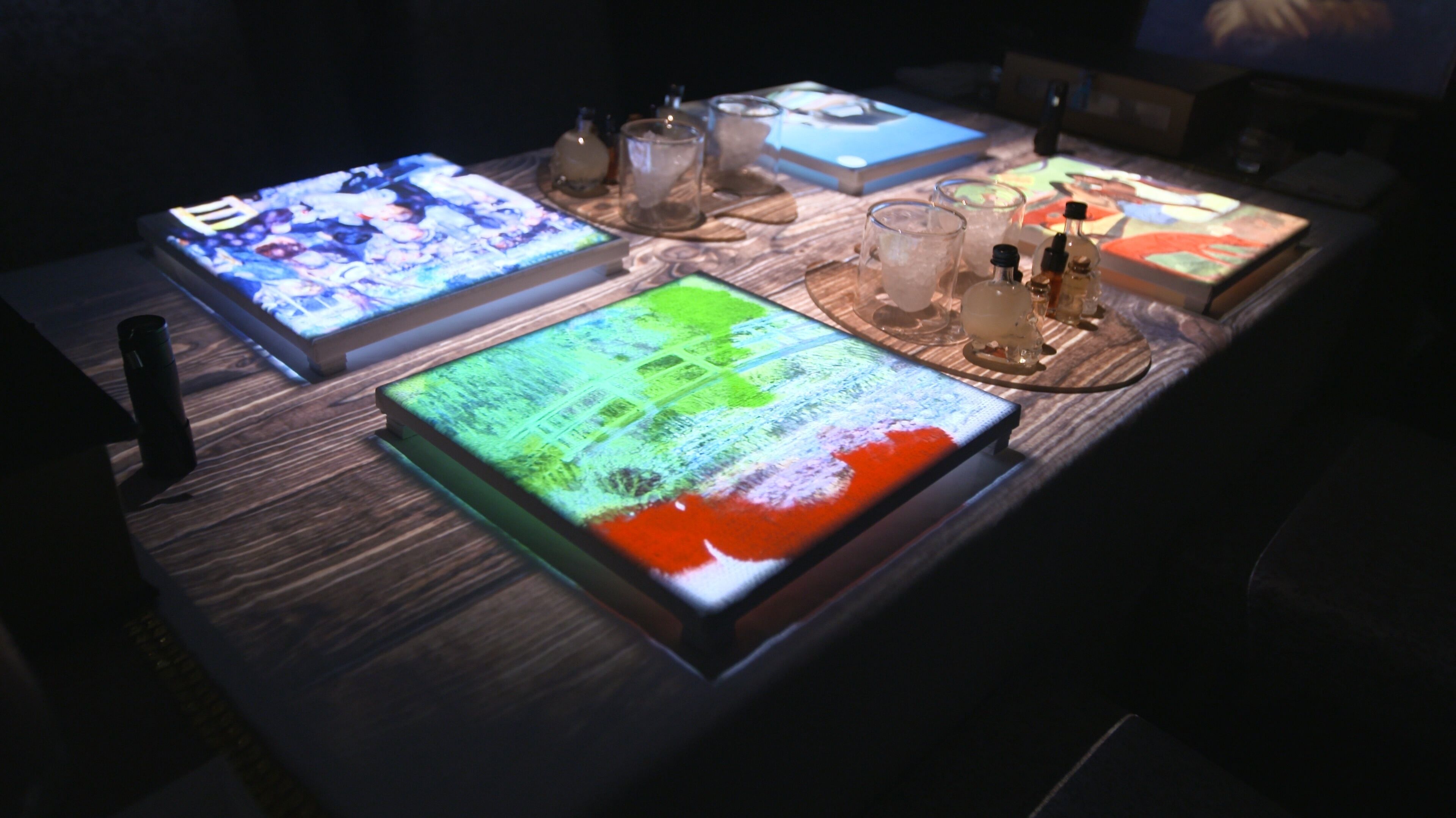A table with electronic devices displaying colorful graphics, a thermos, and a few bottles.