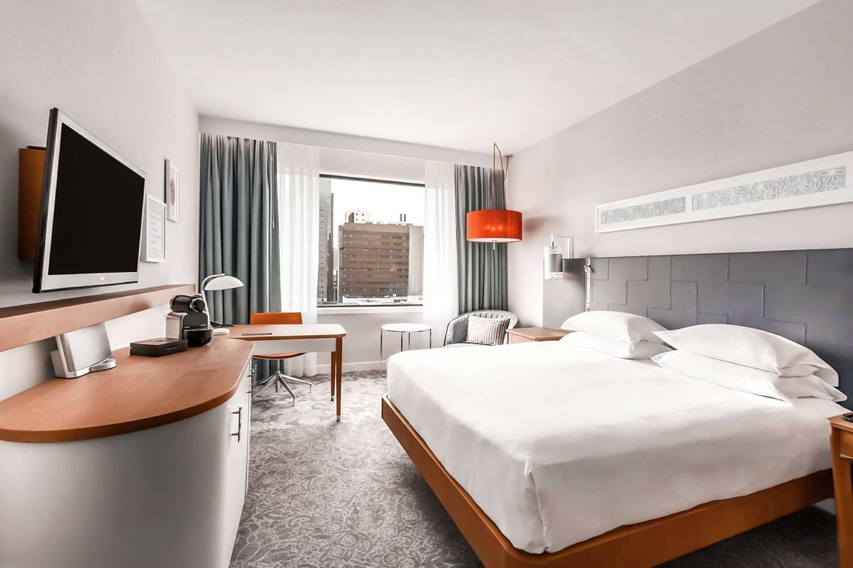 A hotel room with a bed, a desk, a chair, a TV, and a window with curtains.