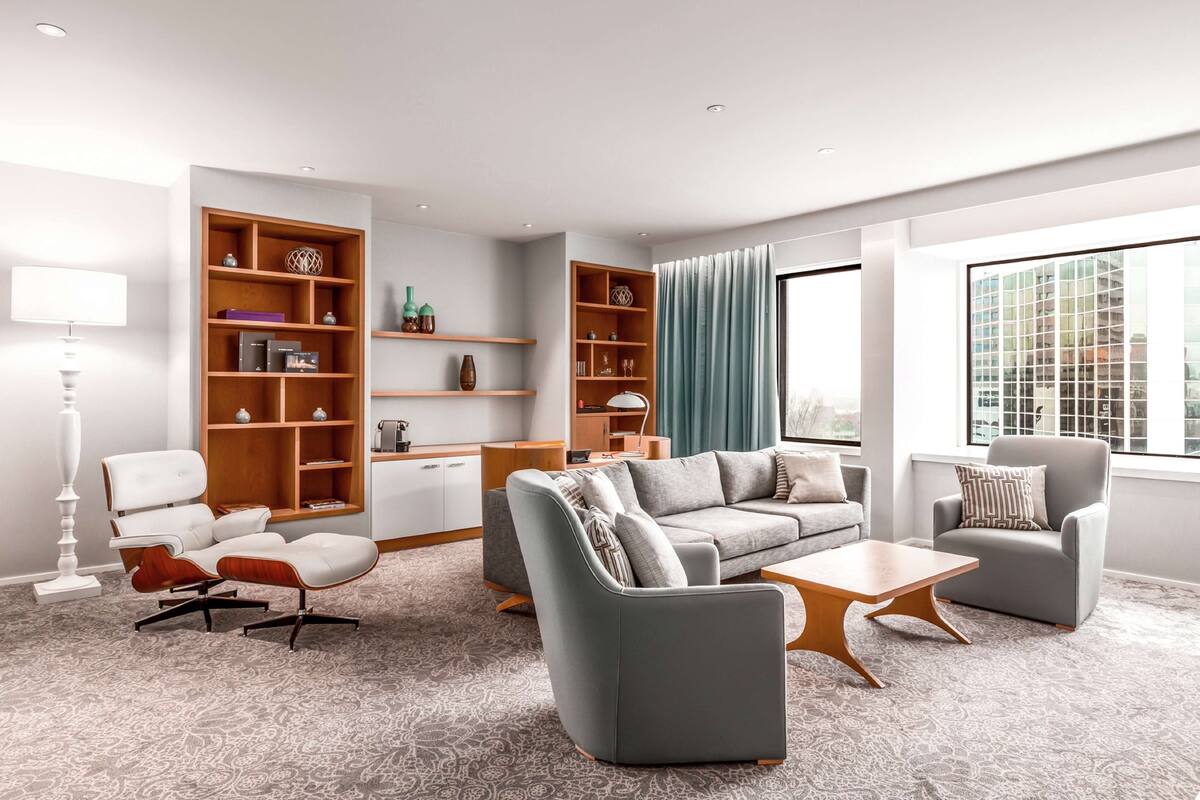 A modern living room with a grey sofa, two armchairs, a coffee table, and built-in wooden shelving with decorative items.