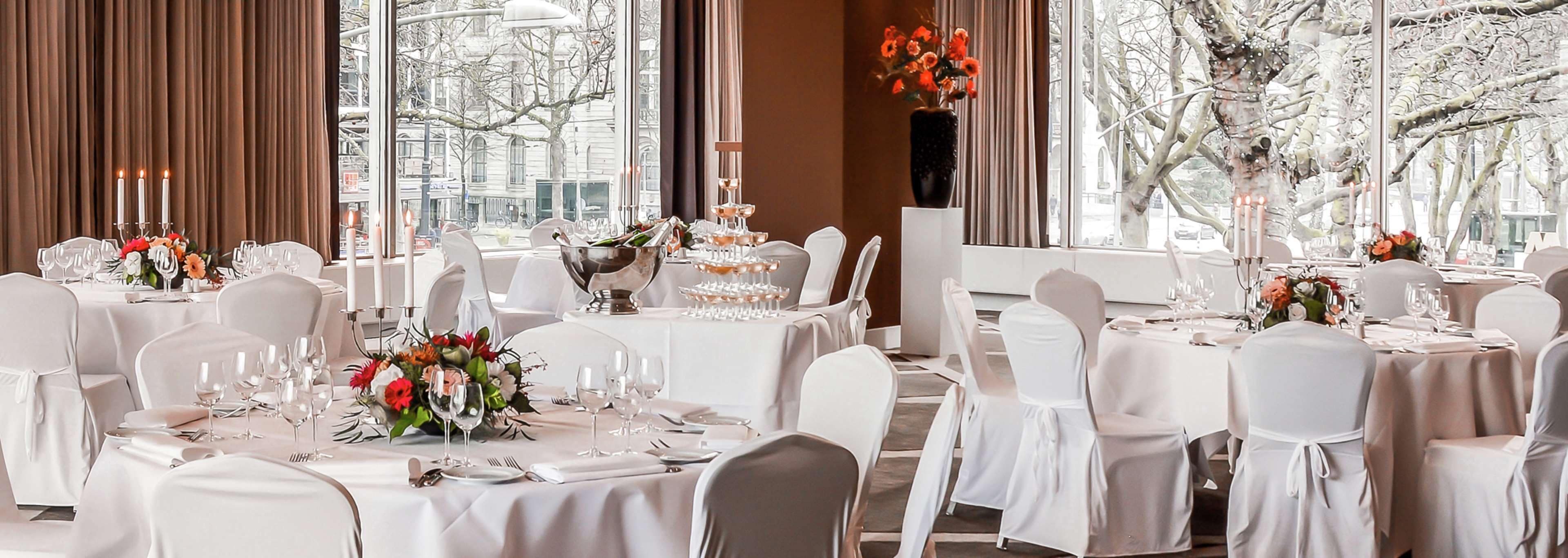 Een balzaal met ronde tafels gedekt voor een formeel evenement, met witte tafelkleden, glazen en bloemstukken.