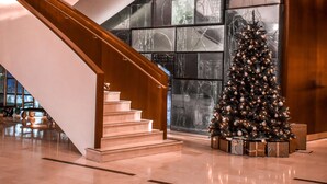 A modern interior with a staircase leading to a second floor, a large Christmas tree, and a reflective glass wall. - Hilton Rotterdam (Rotterdam)