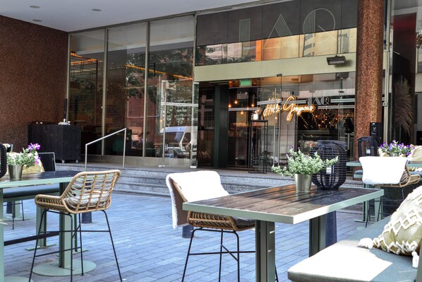 An outdoor seating area with tables and chairs, a glass entrance to a building, and a brick wall. - Hilton Rotterdam (Rotterdam)