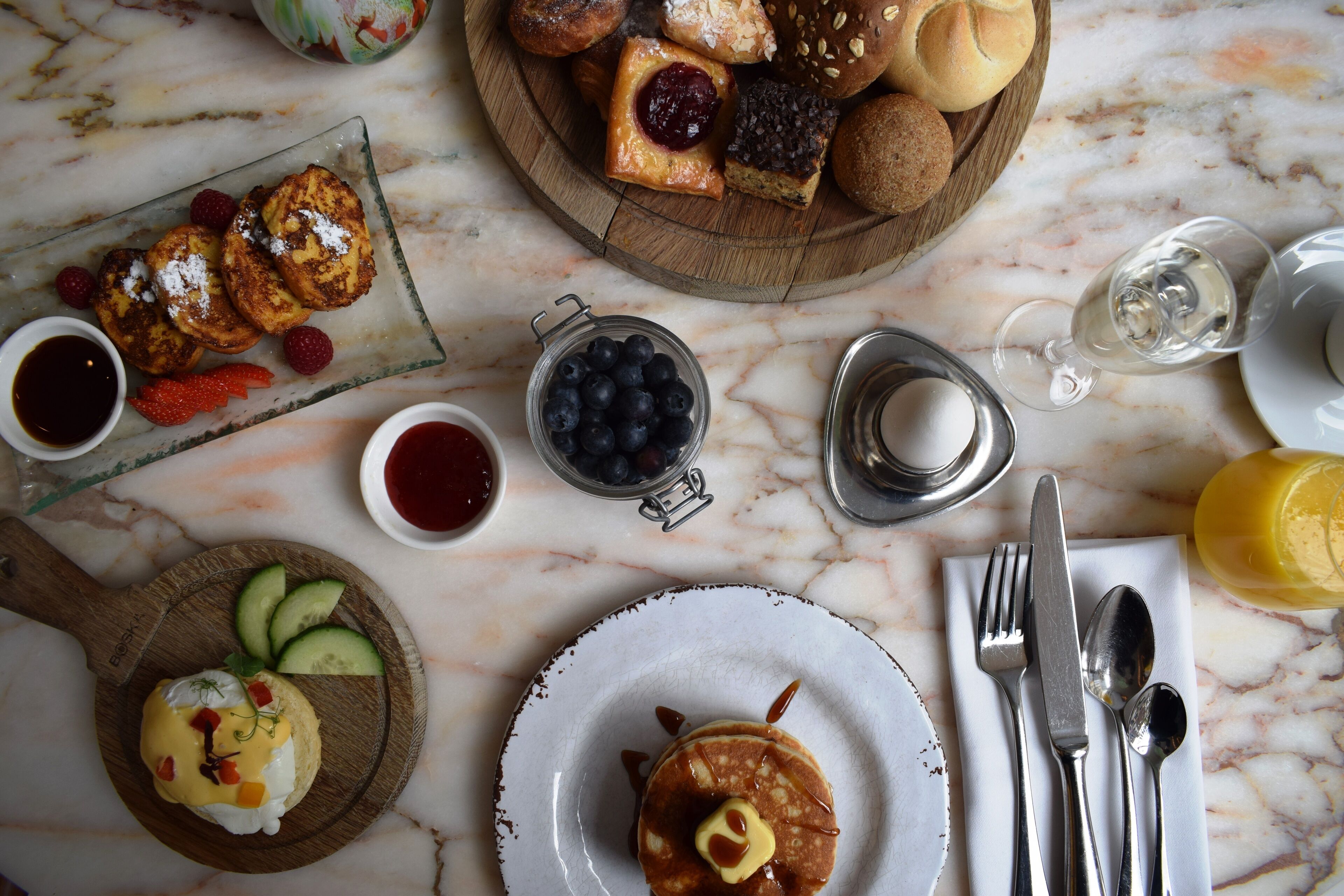 Ein Frühstückstisch mit Pfannkuchen, Gebäck und frischem Obst auf einer Marmortafel.