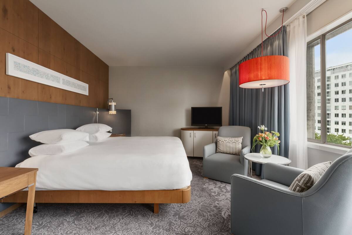 A hotel room with a large bed, a sofa, a TV, and a window with curtains.