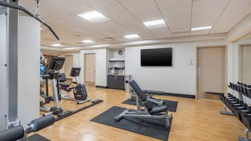 A gym with exercise equipment, a clock, and a TV on the wall.
