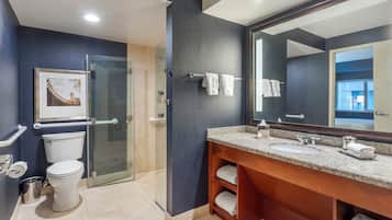 A modern bathroom with a glass-enclosed shower, a large mirror, and a granite countertop sink.