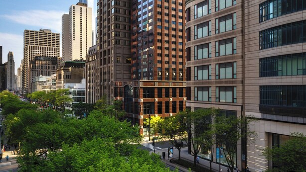 A high-rise building with a modern glass facade, surrounded by other tall buildings and a park area with trees.