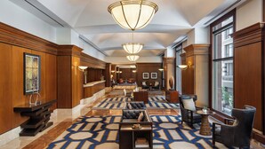 Eine geräumige Lobby mit einem gemusterten Teppich, Holzvertäfelung und modernen Leuchten.