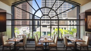 A dining area with tables set for four, large windows with a view of city buildings, and a curved ceiling structure.