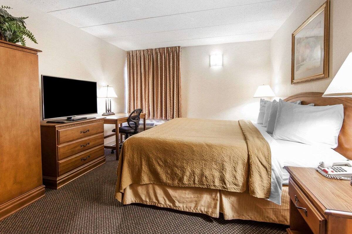 Une chambre d’hôtel avec un grand lit, un bureau avec une télévision, une chaise, une commode et une lampe.