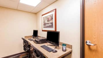 Una oficina de hotel con dos monitores de computadora, una impresora, un teclado y un cuadro en la pared.