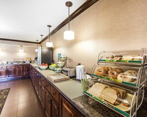 A hotel breakfast area with a buffet setup including bread, pastries, and fruits.