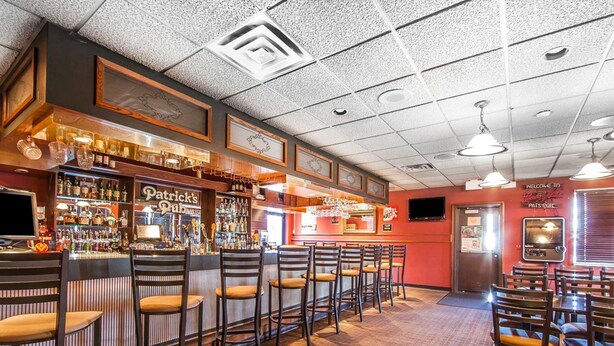 A bar area with wooden bar stools, a counter with liquor bottles, and a television screen. - Quality Inn Chillicothe (Chillicothe)