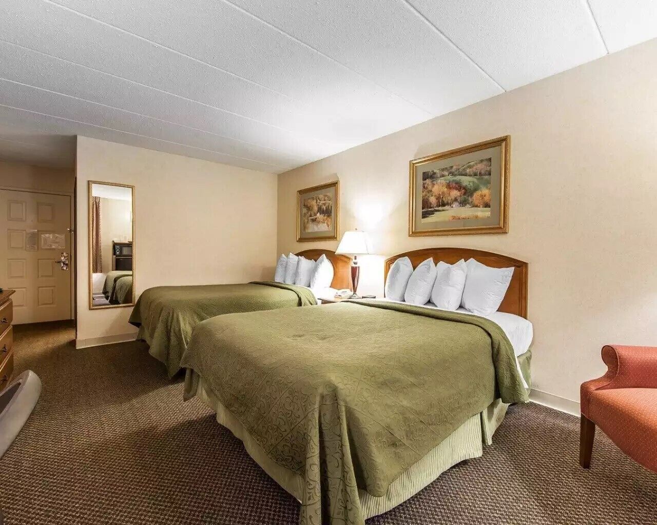Een hotelkamer met twee bedden, een bureau, een stoel, een lamp en een schilderij aan de muur.